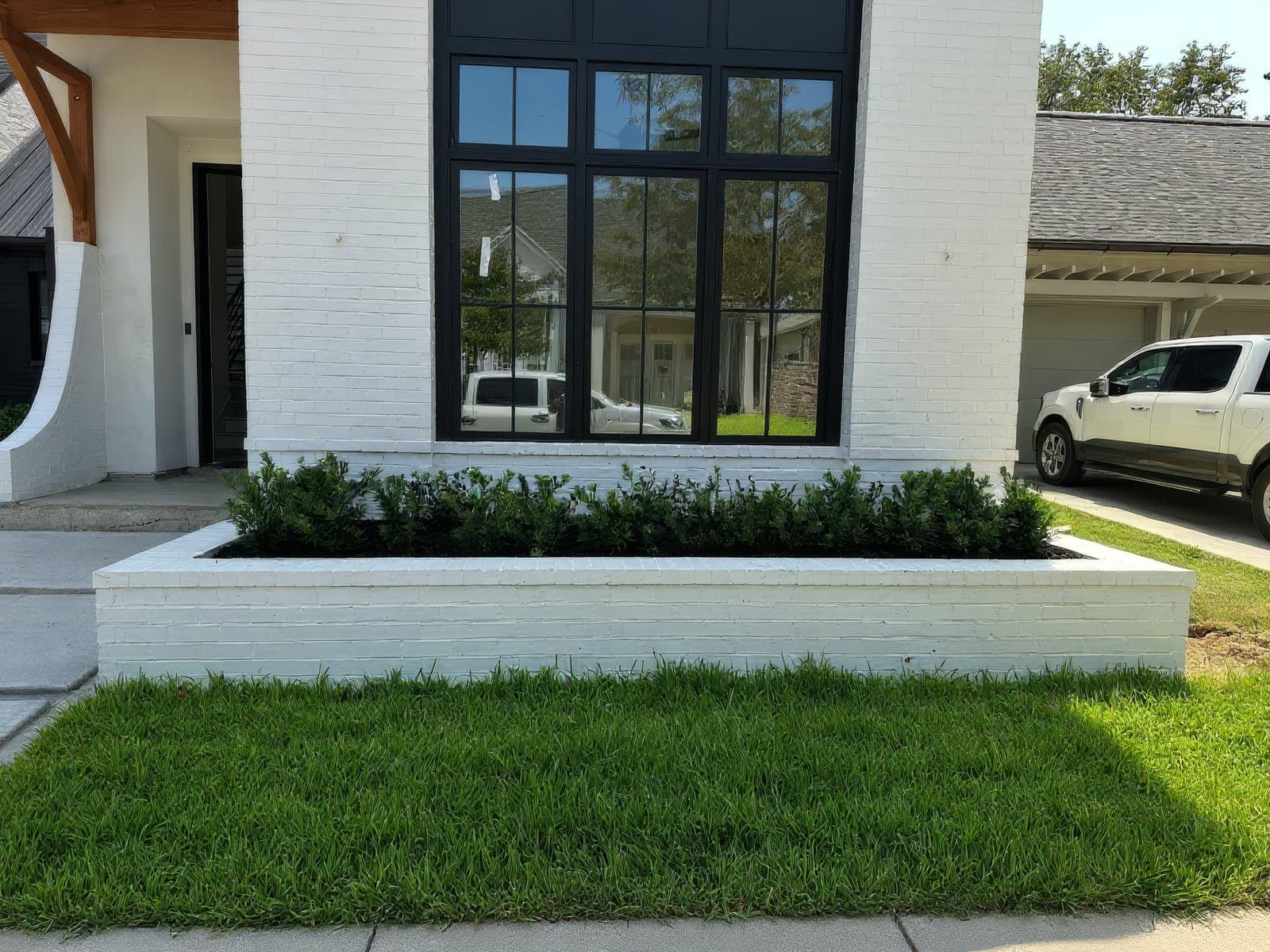 A freshly landscaped front yard with a white brick planter bed filled with newly installed shrubs and lush green sod in front of a modern home