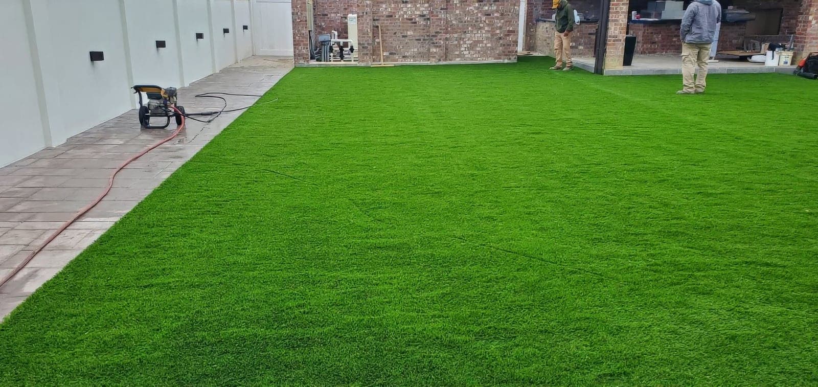 Freshly installed artificial turf lawn in a backyard patio area with workers inspecting the completed installation