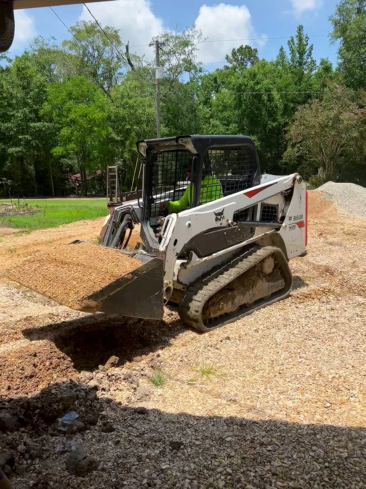 A crew member operating a compact track loader to spread and grade material