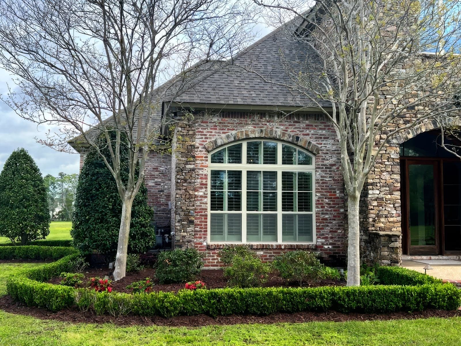 A stone and brick home with trimmed hedges and azaleas