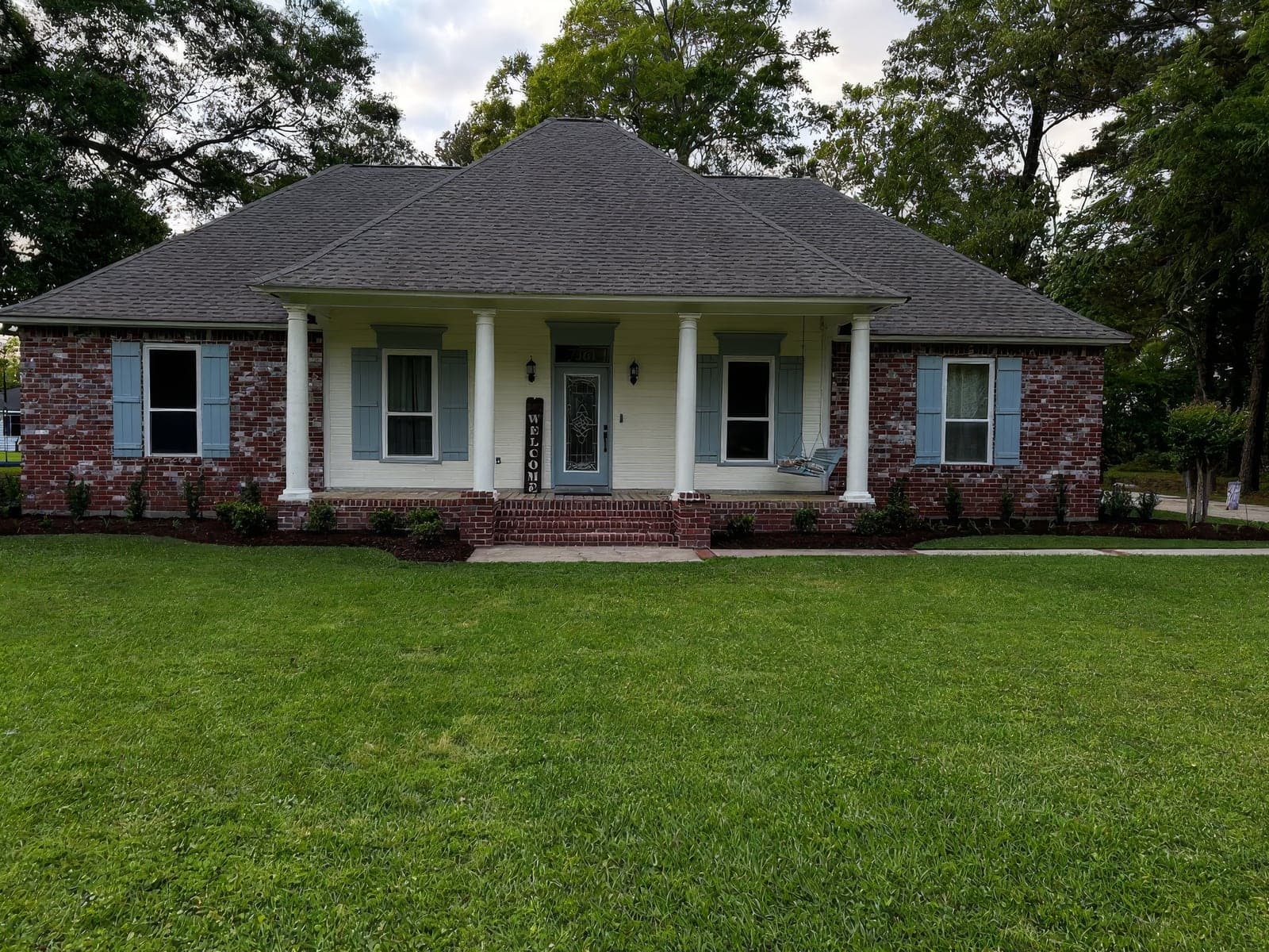 A brick single-story home with light blue shutters and a well-manicured lawn, showcasing landscaping and curb appeal work