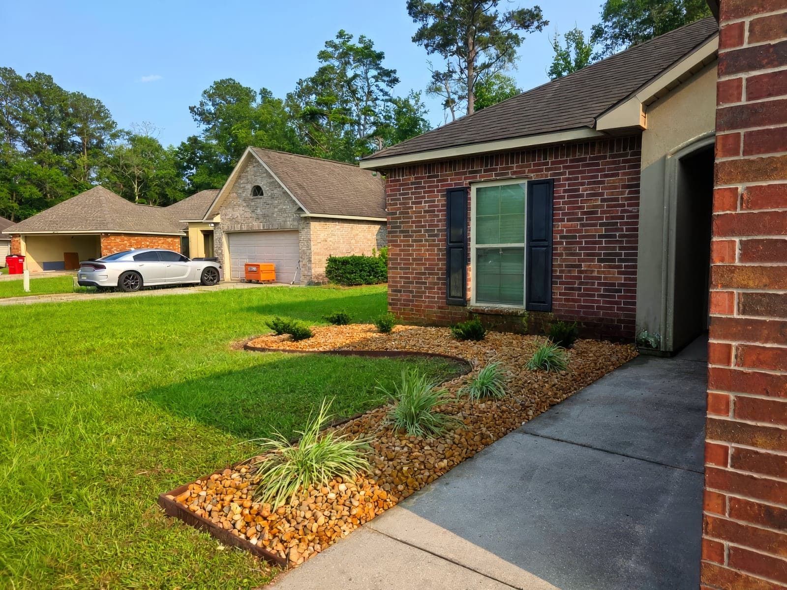 A landscaped front yard bed with decorative rock mulch, ornamental grasses, and clean edging alongside a brick home's walkway