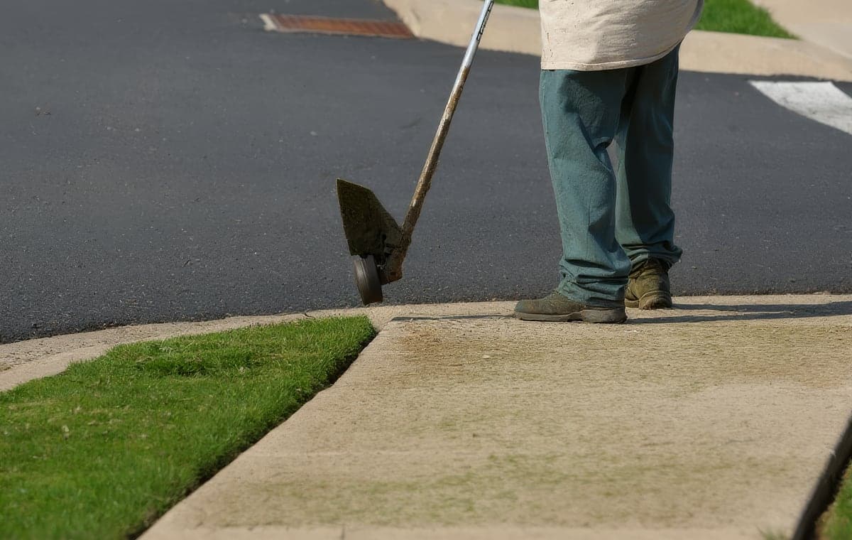 A crew member edging grass along a sidewalk with a stick edger
