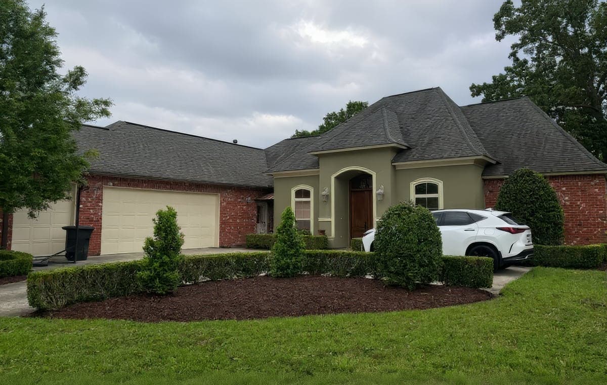 A well-manicured front yard of a brick home featuring neatly trimmed shrubs and fresh mulch beds, showcasing professional landscaping work