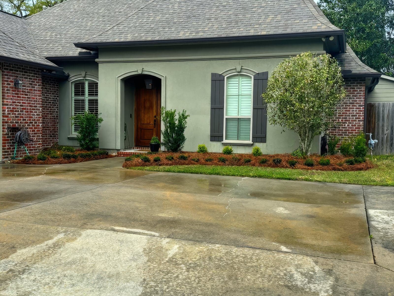 Front exterior of a stucco and brick home with freshly landscaped flower beds, mulch, and newly planted shrubs along the walkway
