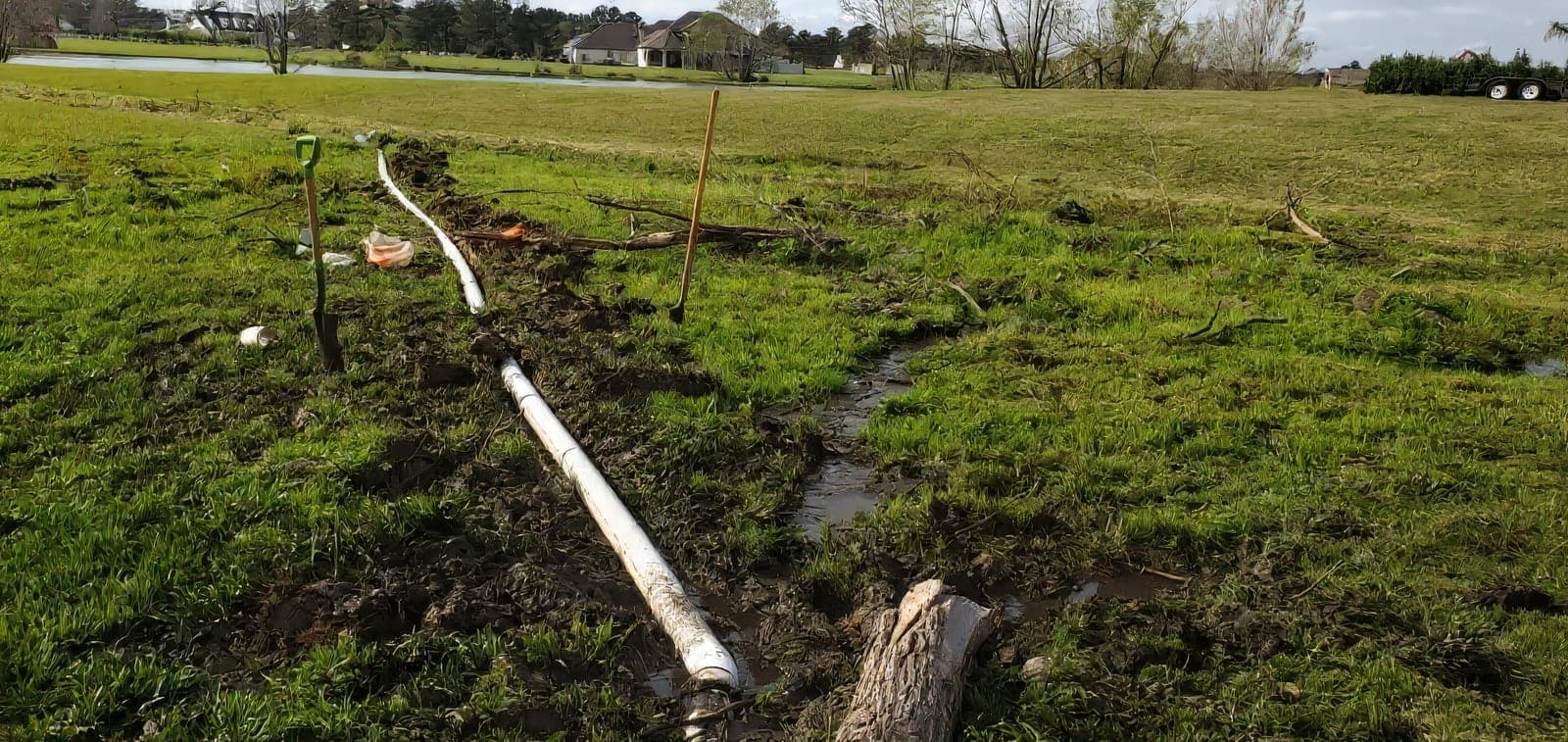 White PVC irrigation pipe laid along a fresh trench across an open lawn