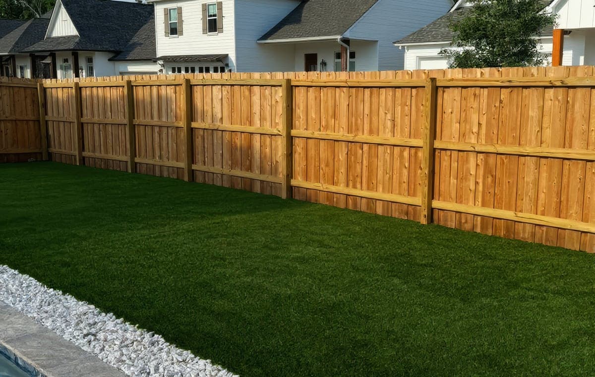 A new cedar privacy fence beside freshly laid artificial turf edged with white rock