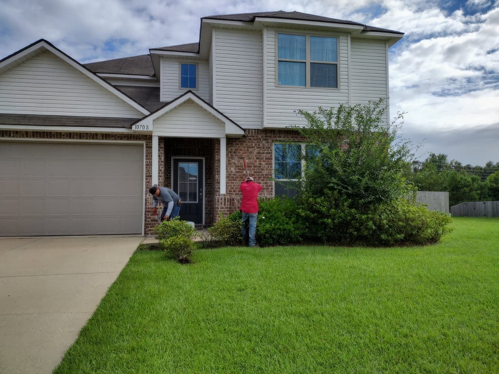 Two crew members tending the beds in front of a two-story brick and siding home
