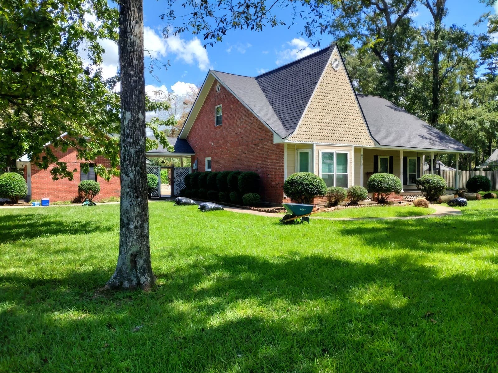 A brick and tan-sided home with a wraparound porch and round shrubs