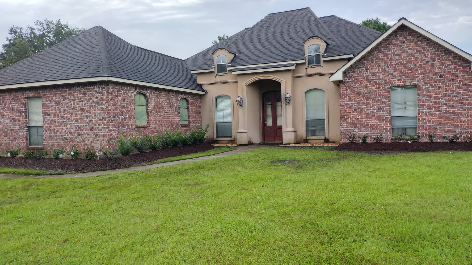 A brick and stucco home with new shrubs and dark mulch beds