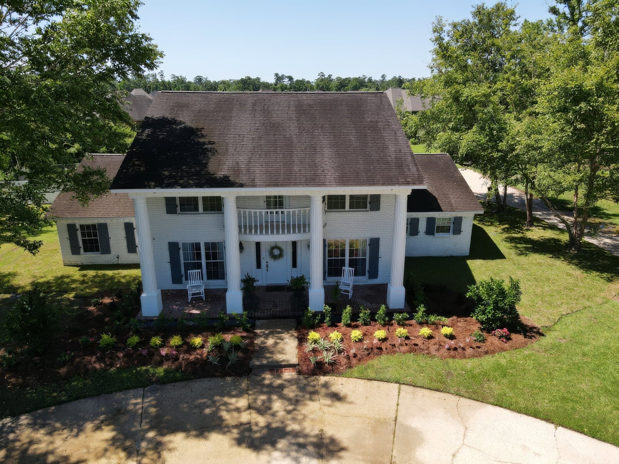 Aerial view of a white two-story brick home with a columned porch and fresh pine straw beds