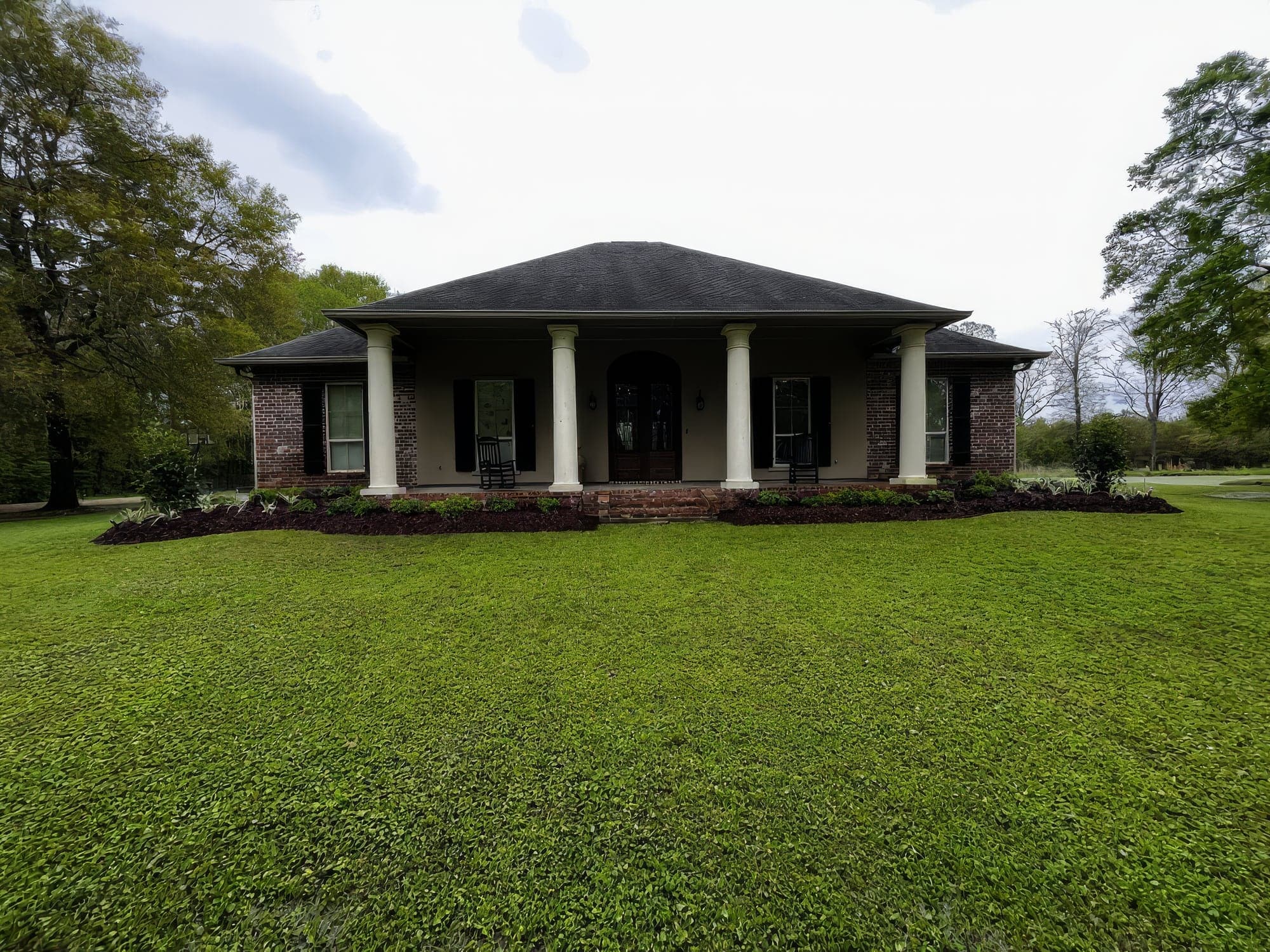 A brick home with a columned porch, rocking chairs and a freshly mowed lawn