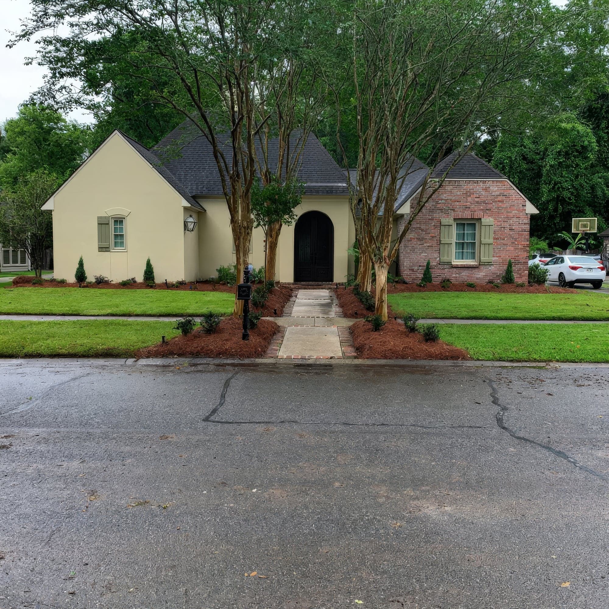 A cream stucco home with crape myrtles and pine straw beds