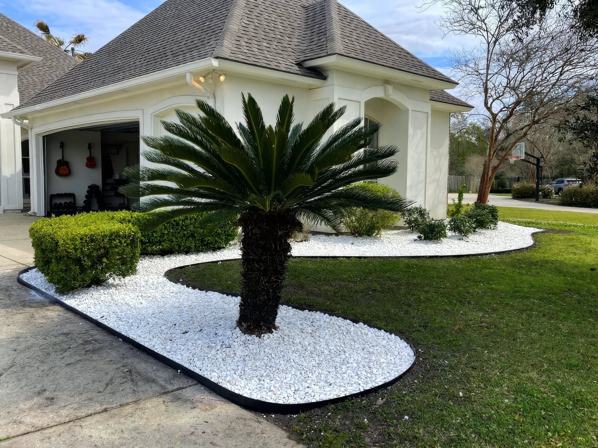 A white decorative rock bed with black edging and a sago palm centerpiece