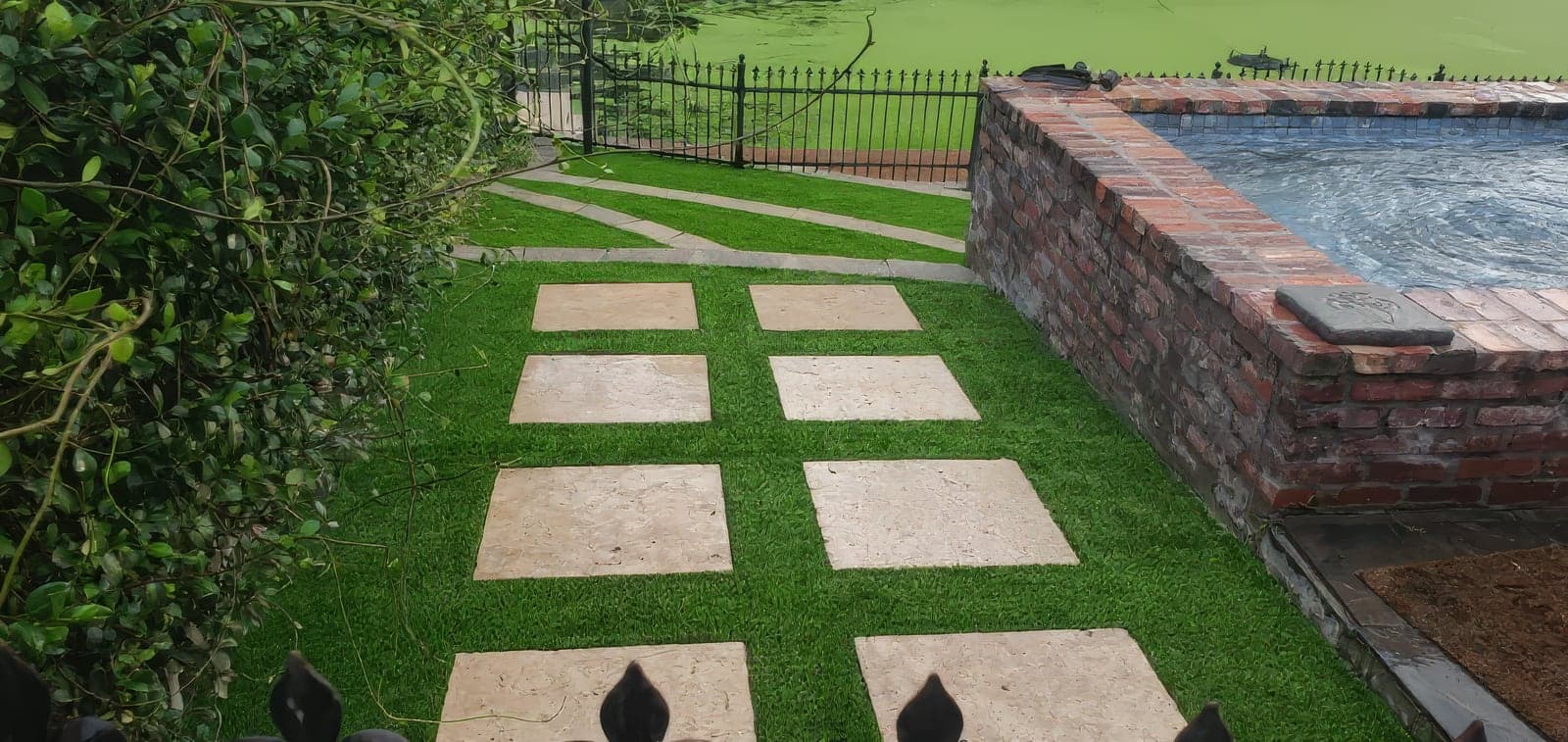 Square stone pavers set in artificial turf beside a brick-edged spa