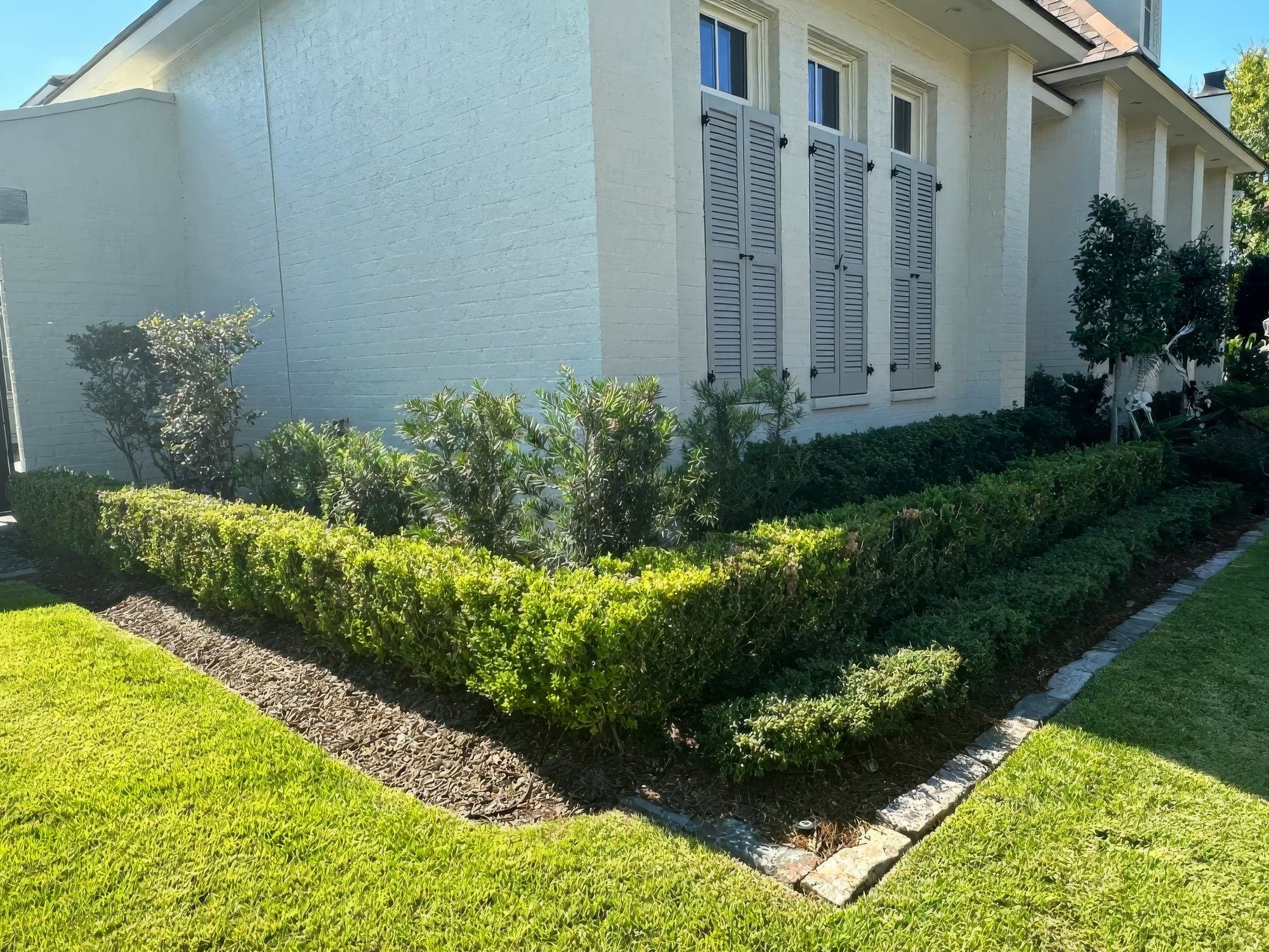 Freshly manicured boxwood hedges with stone edging along a white brick home