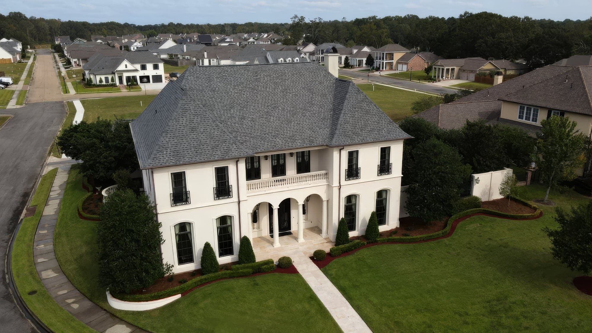 Aerial view of a two-story white Baton Rouge home with a manicured lawn, sculpted hedges and fresh red mulch beds installed by Hernandez Lawnscape