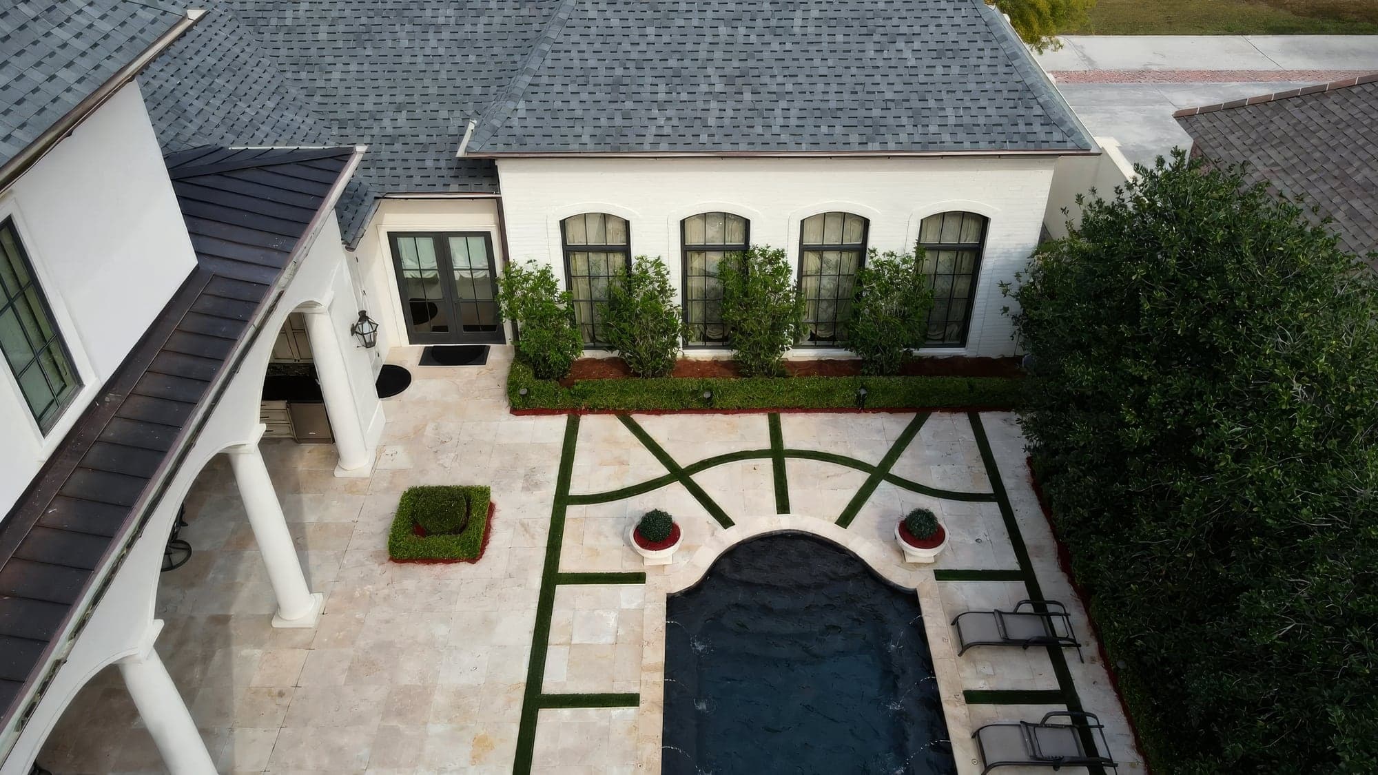 Aerial view of a travertine courtyard with a curved pool and geometric grass joints