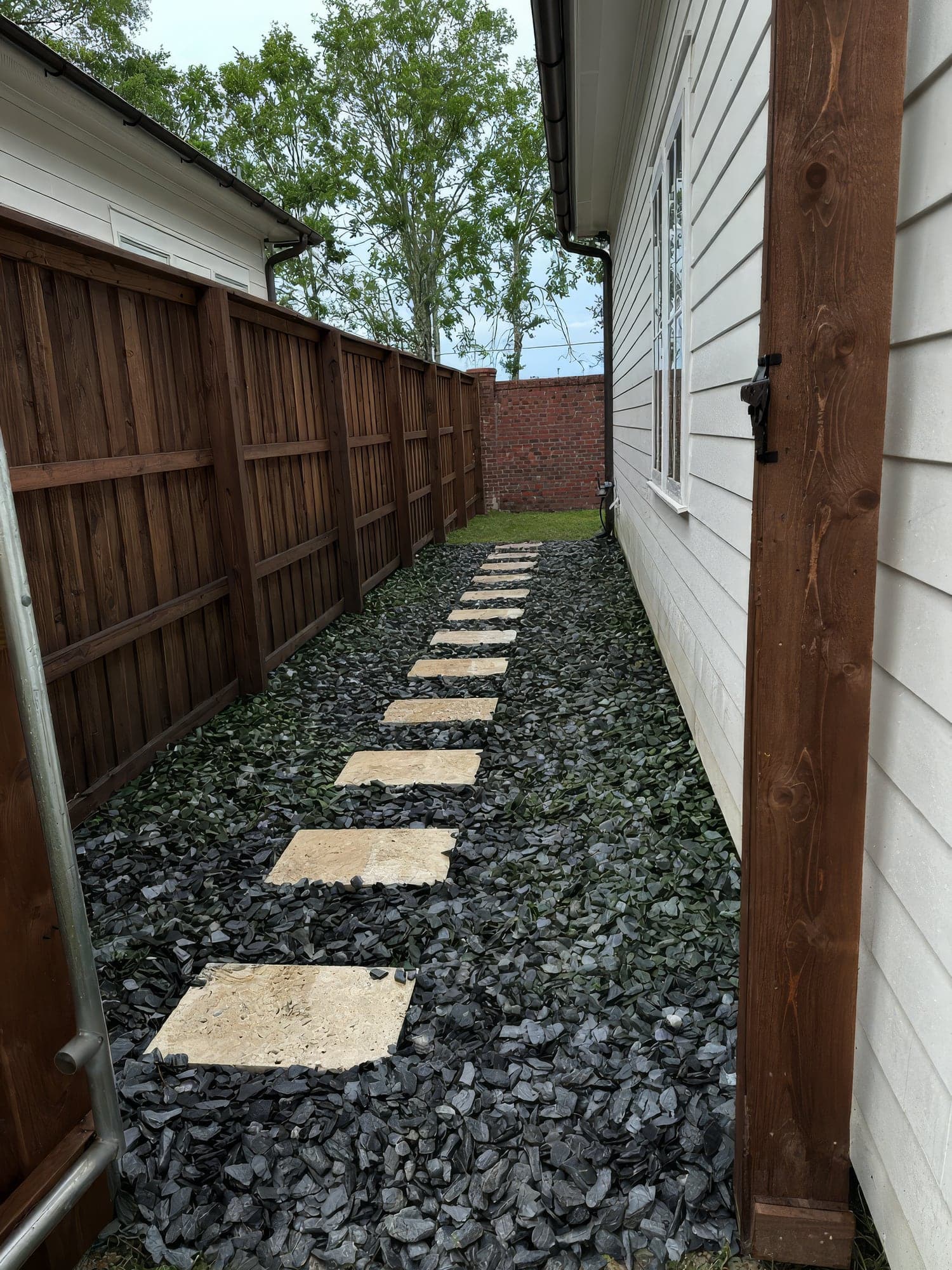 Travertine stepping stones set in dark slate gravel along a narrow side yard
