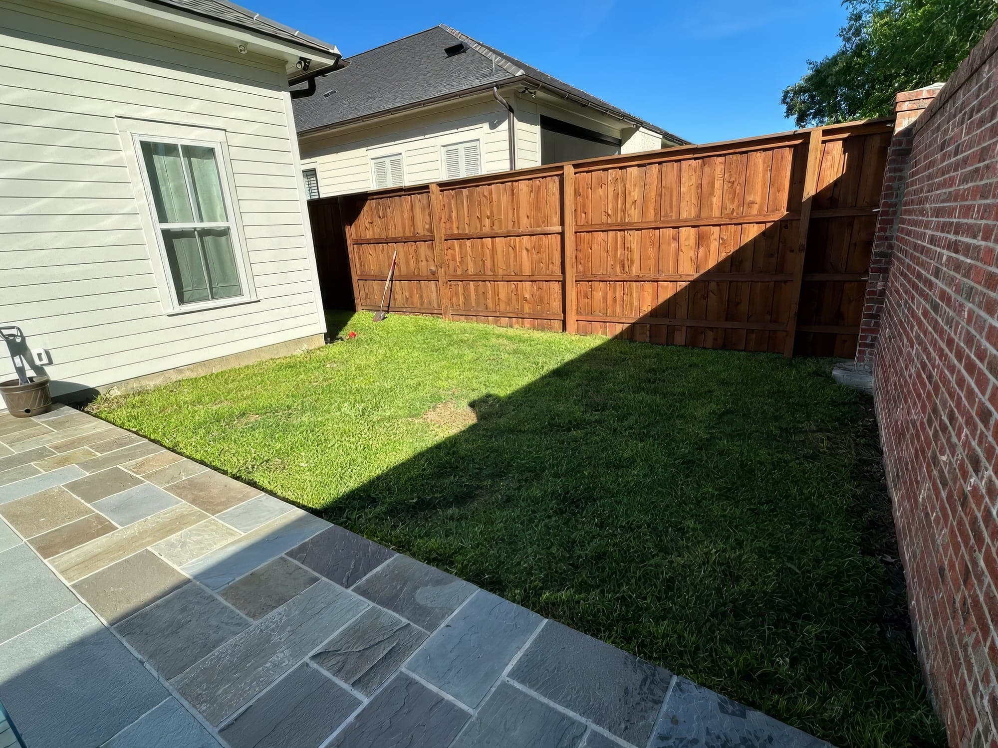 A freshly installed lawn bordered by a new fence, a brick wall and a flagstone patio