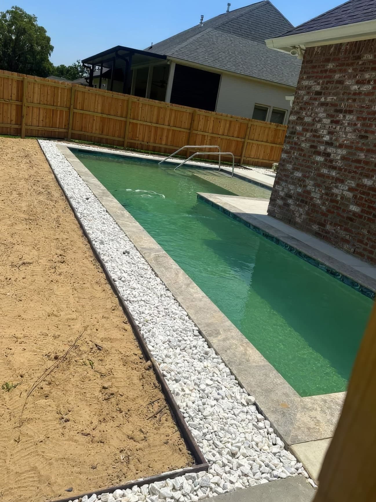 A dirt strip beside a pool before artificial turf