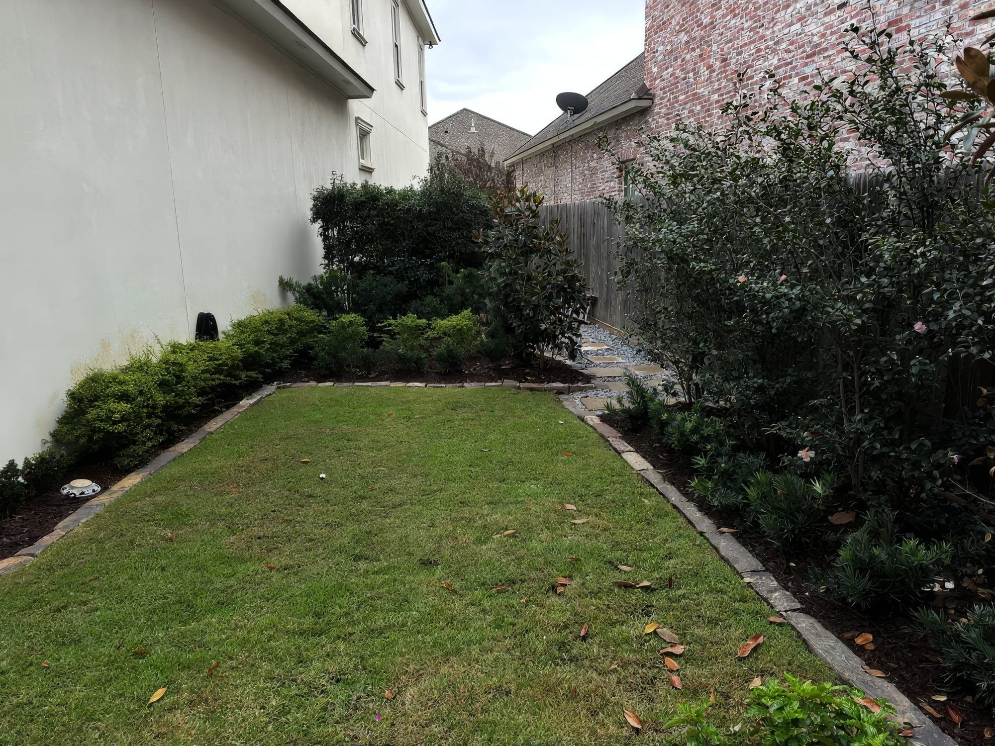 A side yard lawn with edged beds between two brick homes