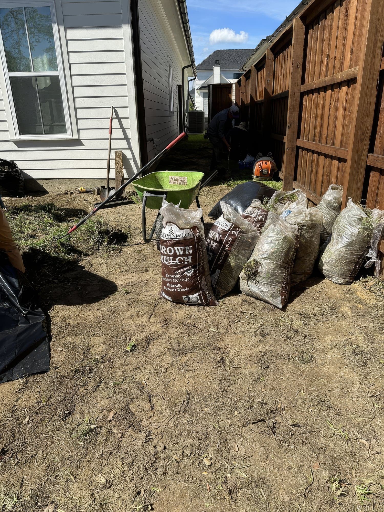 Bags of pulled weeds and debris staged beside a fence during a backyard cleanup