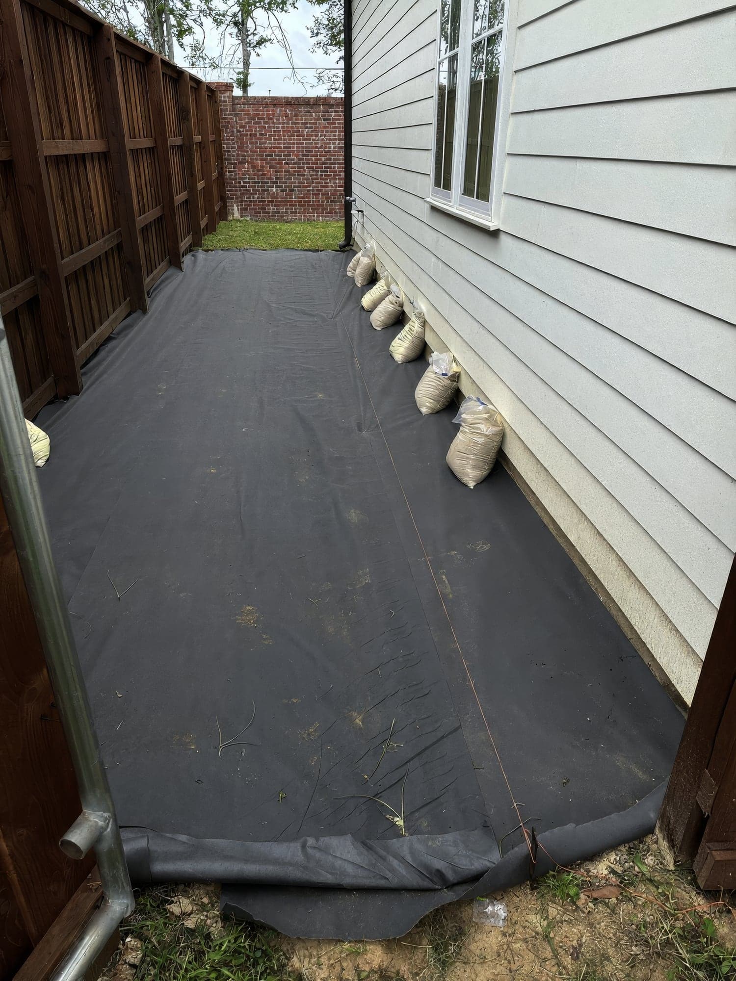 Weed barrier fabric laid along a side yard before gravel and stepping stones