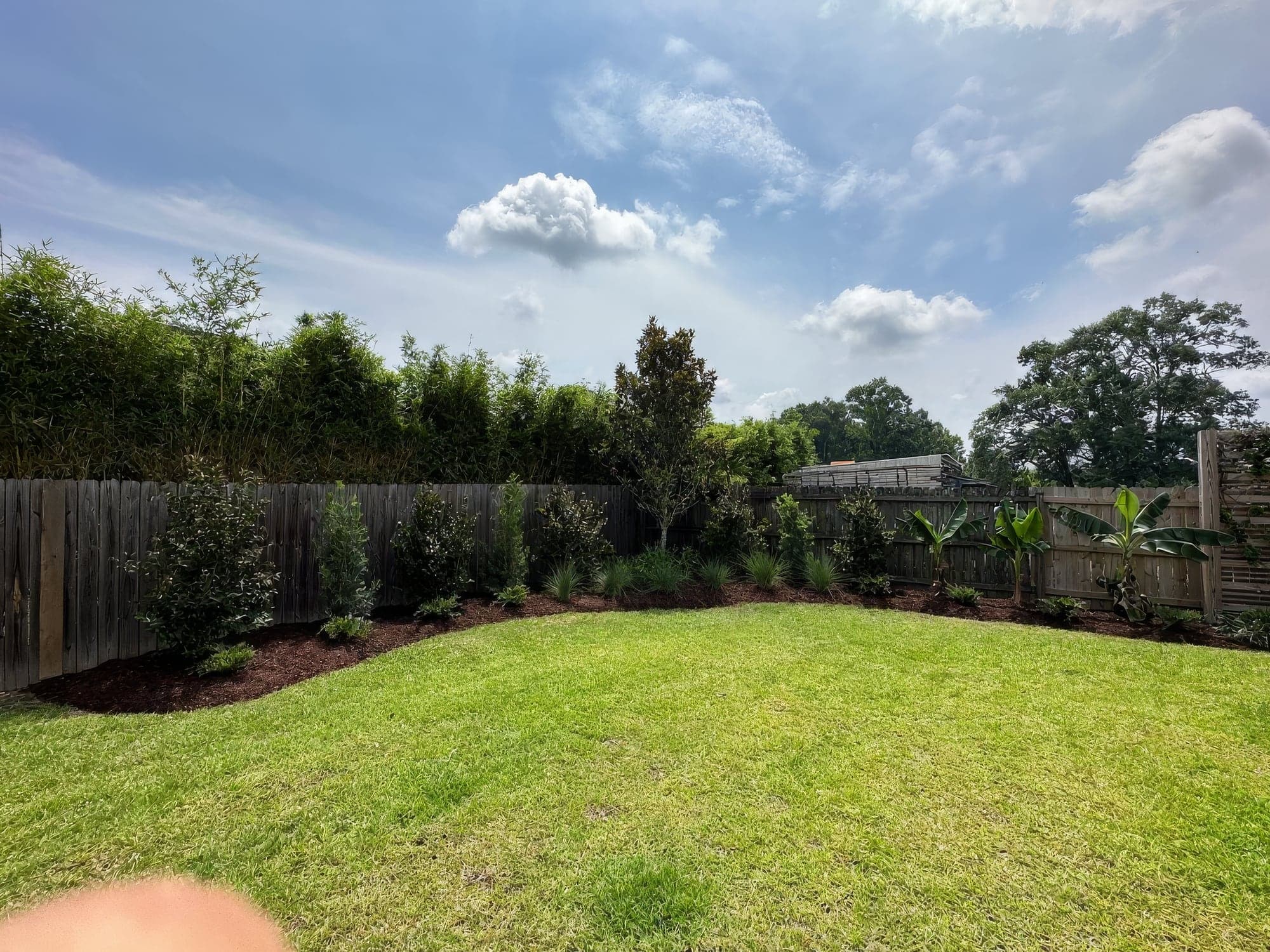 A backyard lawn with a new mulched bed along the fence
