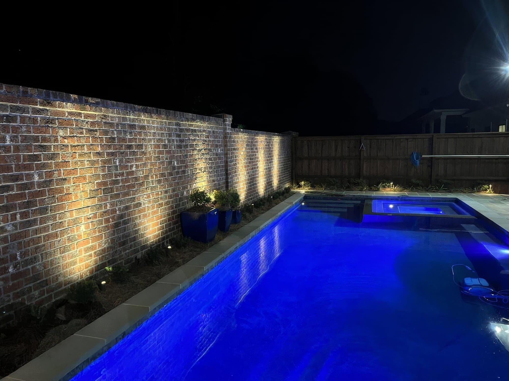 Uplights on a brick wall beside a pool at night