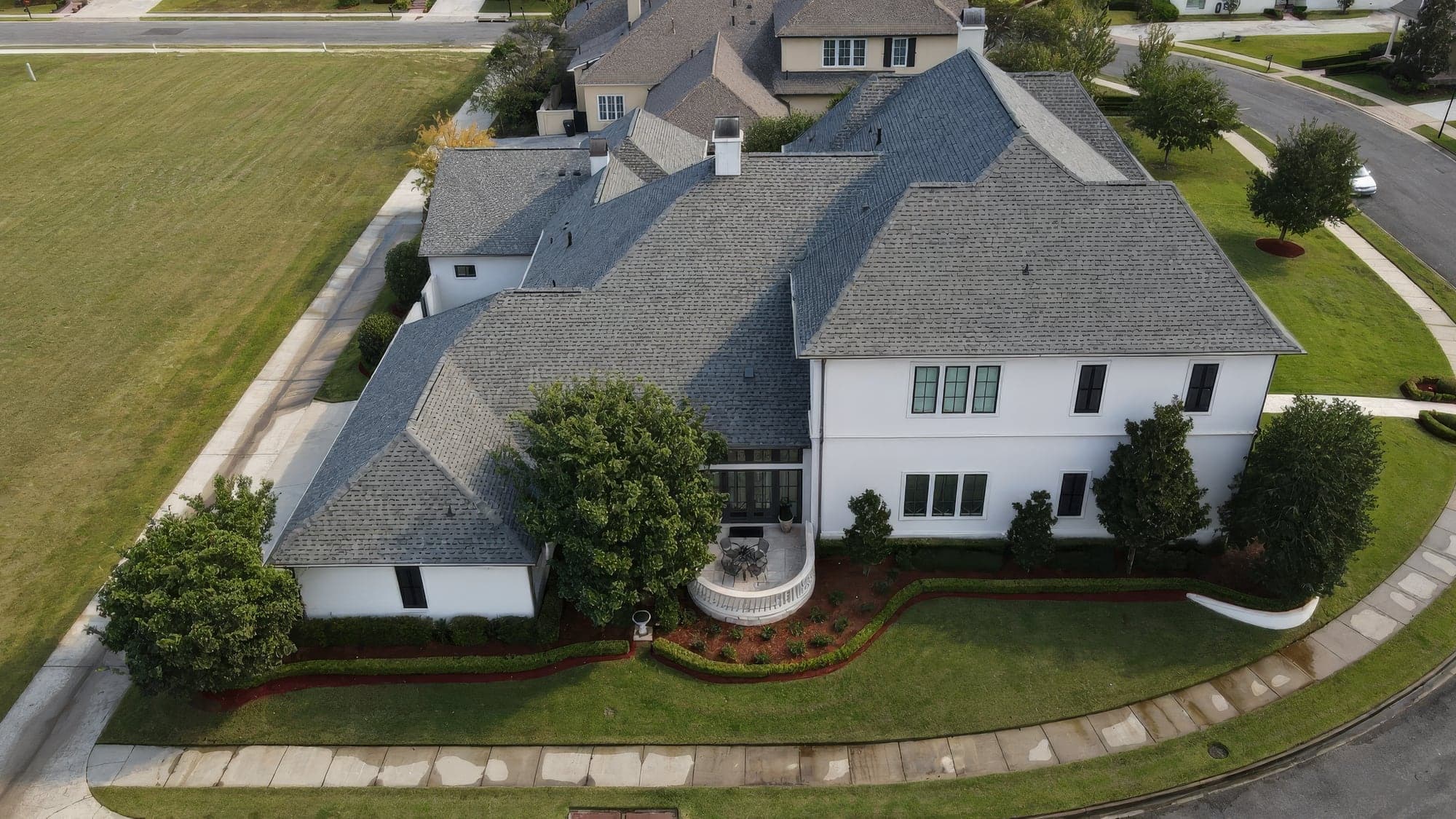 Aerial view of the side of a white estate home with clipped hedges and red mulch