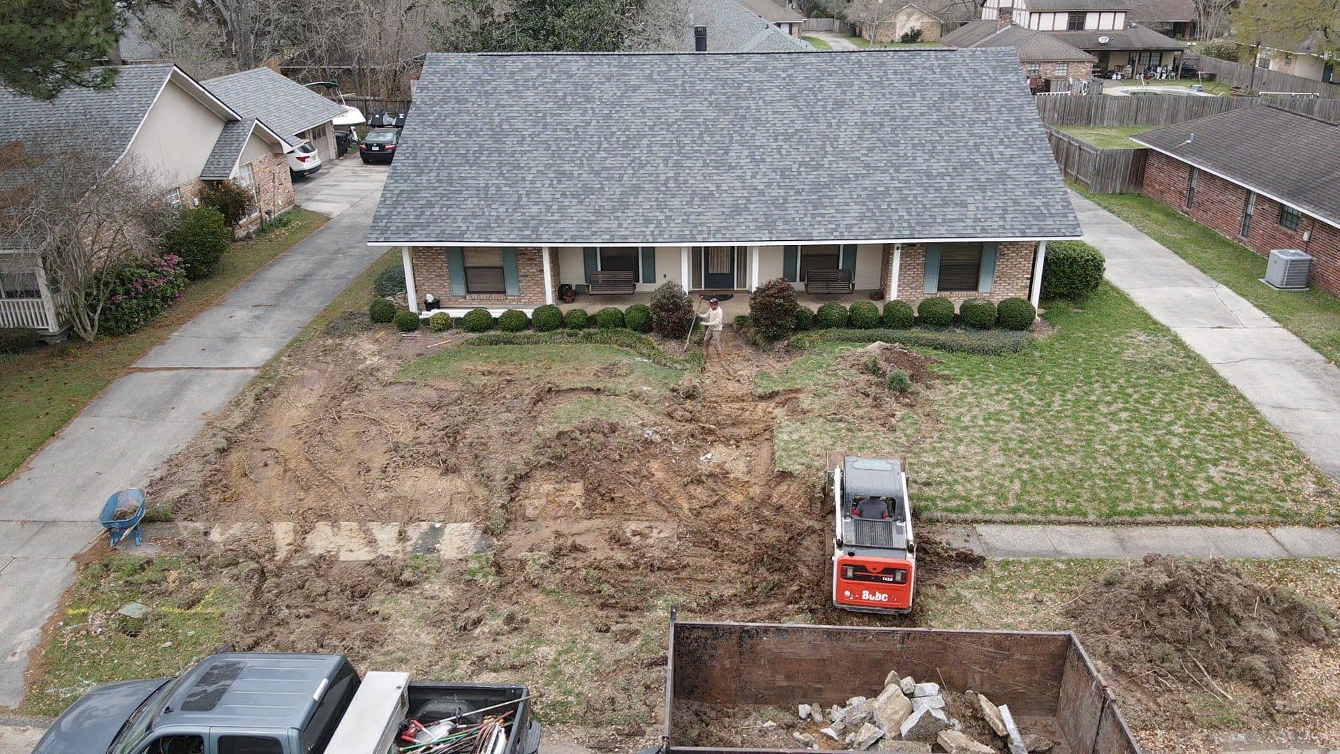 Aerial view of a front yard stripped to soil with a dump trailer