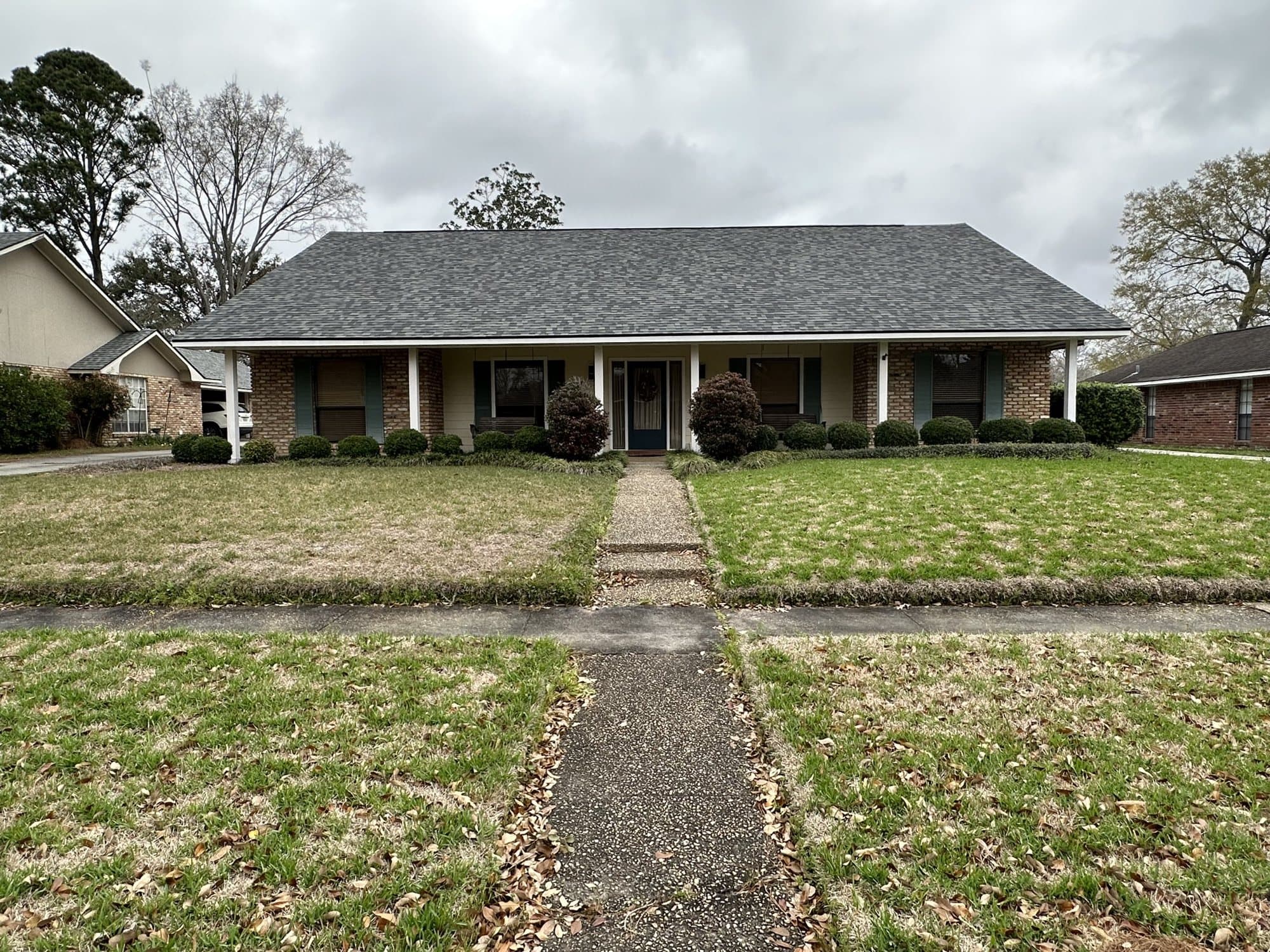 A ranch home with a patchy, weed-filled front lawn before replacement