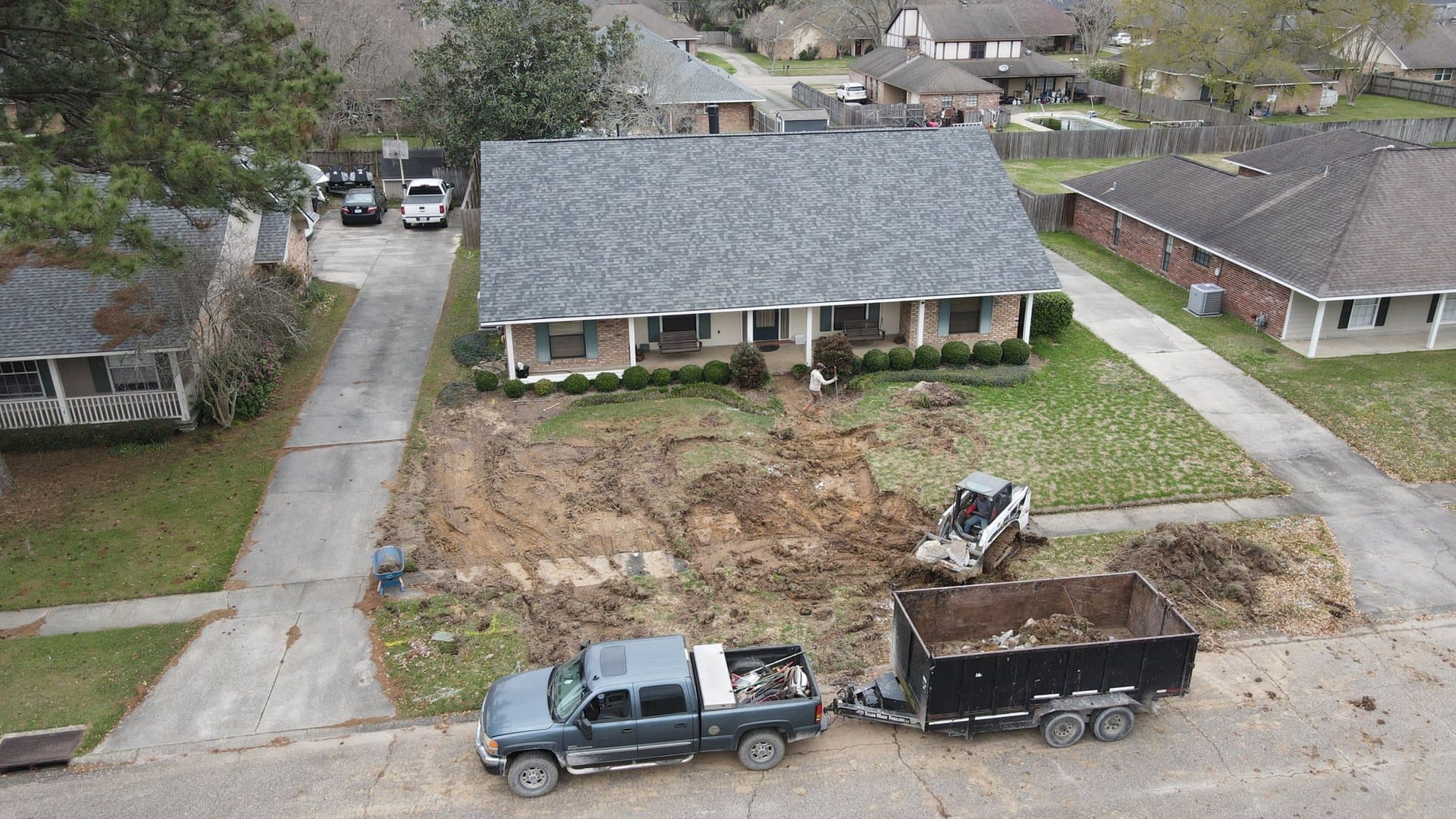 Aerial view of a front lawn stripped to soil with trucks and a trailer