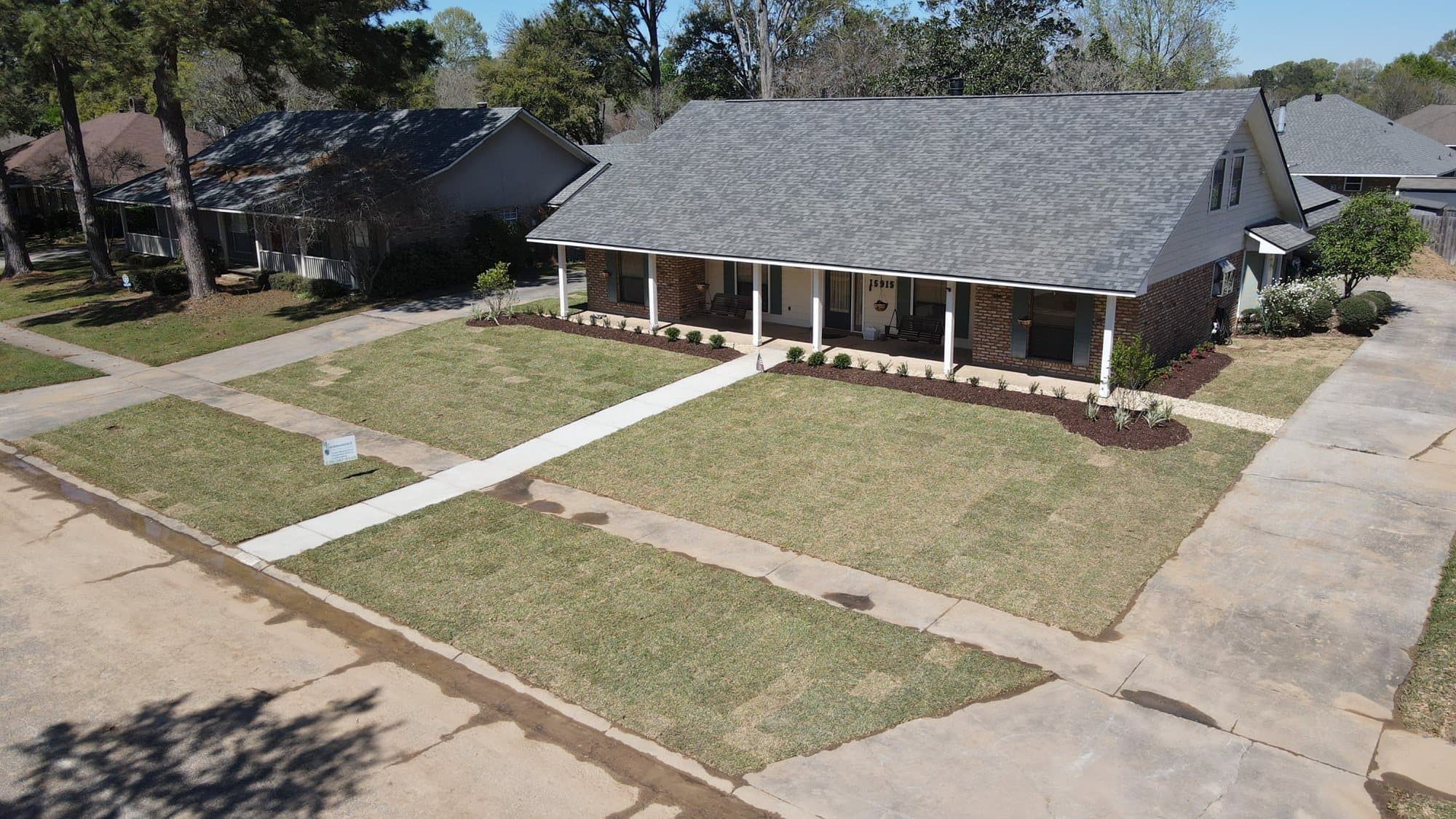 Aerial view of a brick ranch home with a freshly sodded front lawn split by the front walk